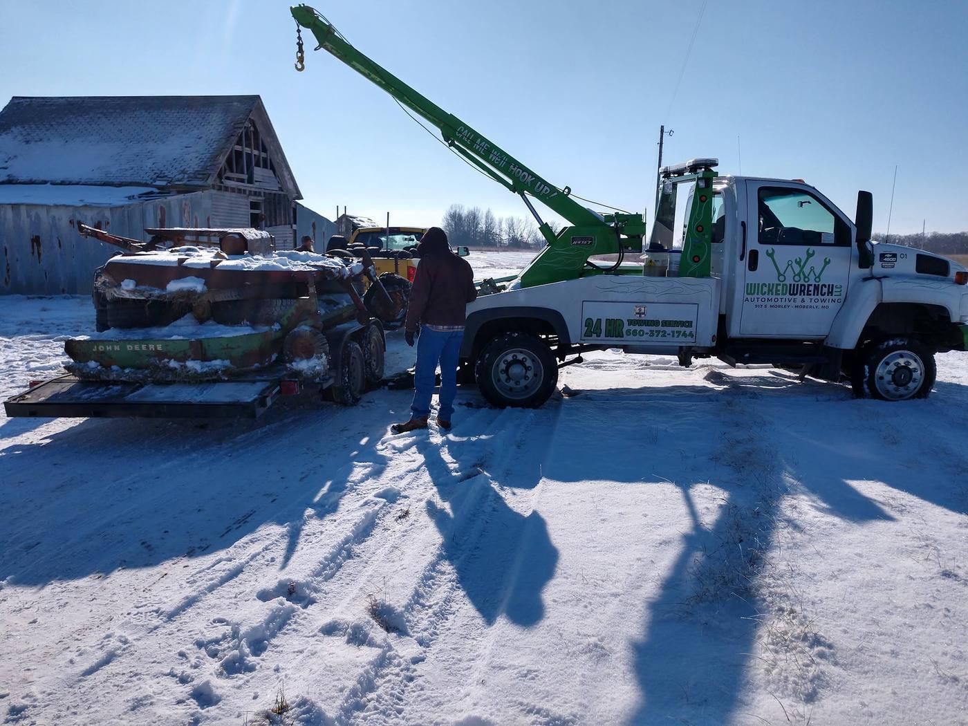 Wicked Wrench boom wrecker lifting farm equipment onto a trailer in the snow